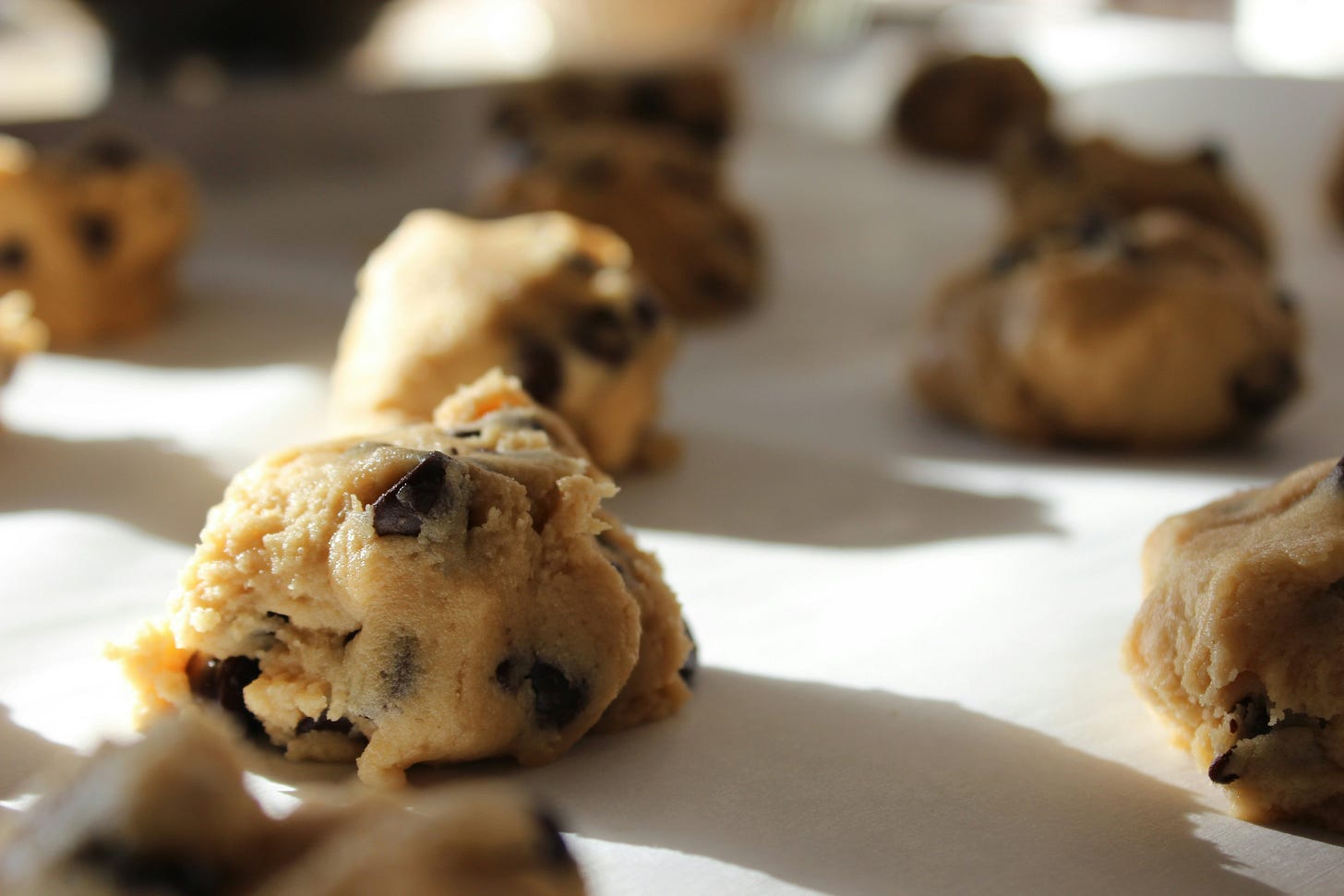 Unbaked round balls of chocolate chip cookie dough on baking parchment