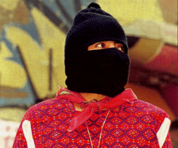 Photograph of a figure wearing a red woven top and black balaclava