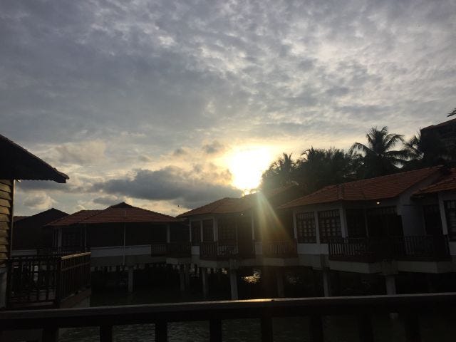 The sun peeking out from behind a row of houses with a dark grey sky. The sun peeking out from behind a row of houses with a dark grey sky.