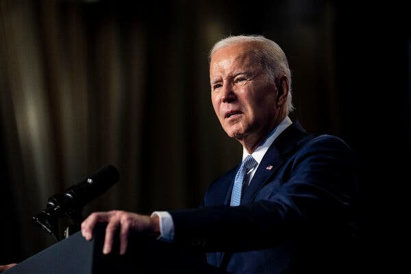 President Joe Biden wearing a blue suit with a blue tie against a dark background. President Joe Biden wearing a blue suit with a blue tie against a dark background.