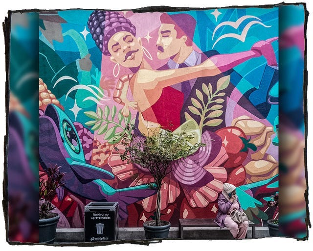 Photo of a sreet mural featuring two dancers. A woman is sitting on a bench in front of the mural.