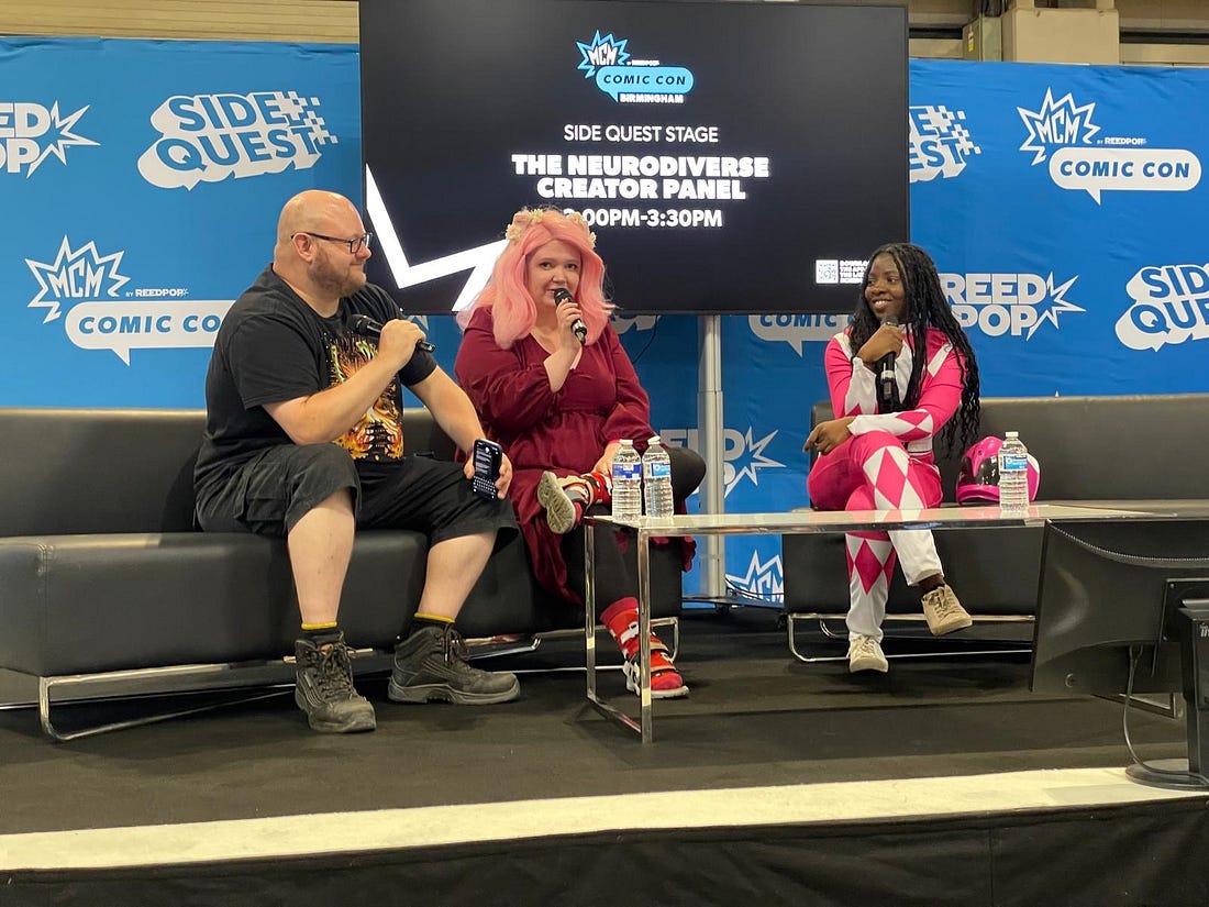 Myself and 2 panel members sat on a couch holding microphones on stage at comic con