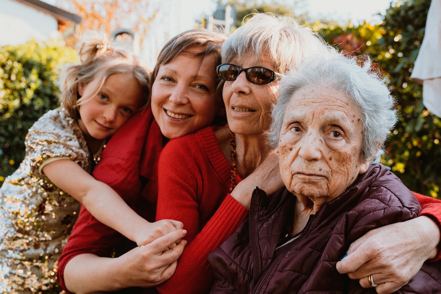 4 generations of women hugging with the oldest woman looking straight to camera with a serious expression