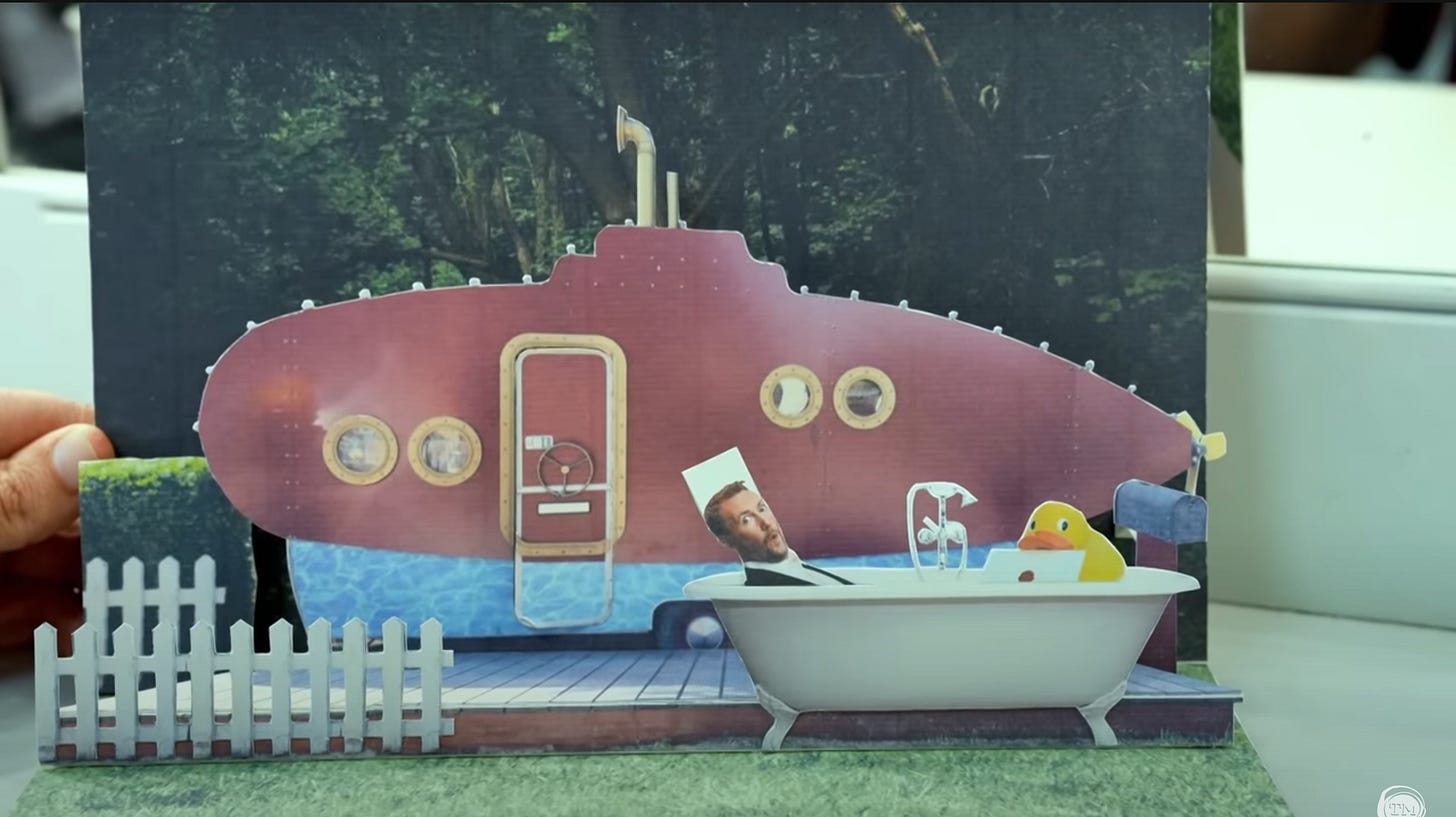 Close-up of a pop-up book with Little Alex Horne popping up in a clawfoot bathtub in front of the submarine-decorated caravan on the Taskmaster grounds.