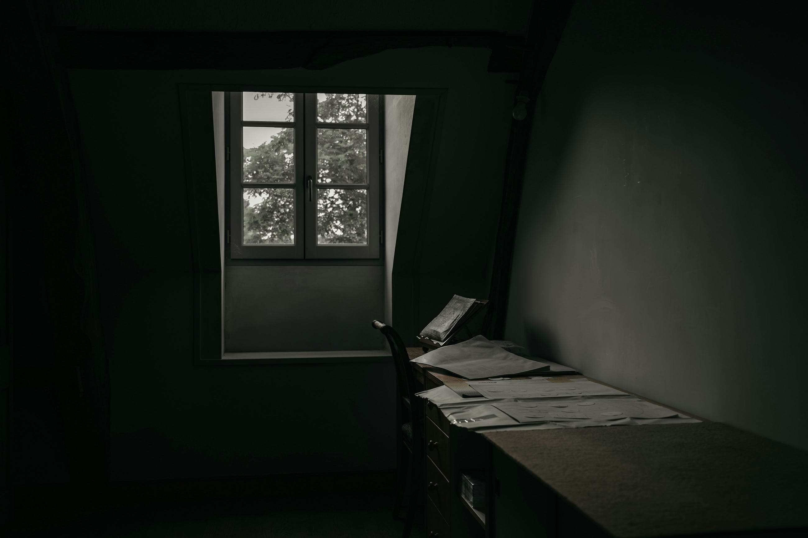 A dark room with papers on a desk and a paned window — black and white photo A dark room with papers on a desk and a paned window — black and white photo