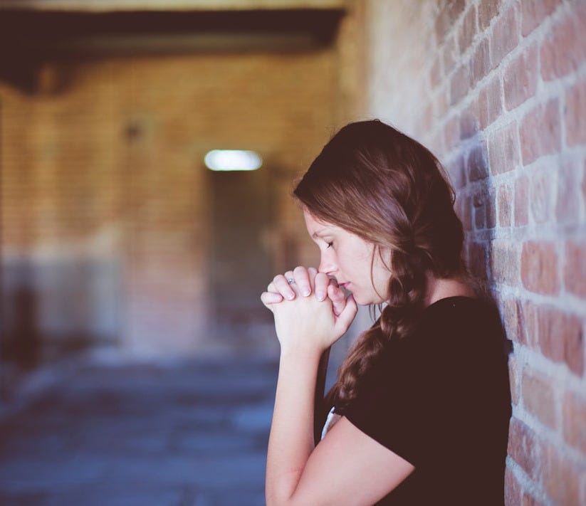 woman praying while leaning against brick wall woman praying while leaning against brick wall