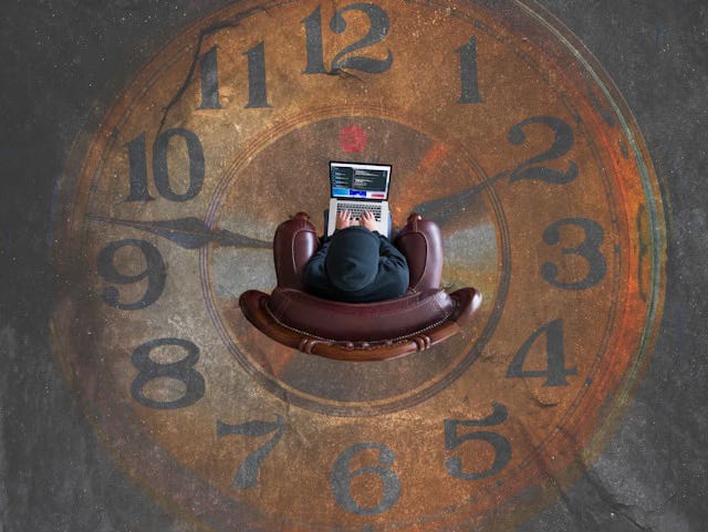 Aerial view of a person sitting in a leather armchair working on a laptop, positioned at the center of a large clock face painted on the ground, evoking the pressure of time management and how creative capacity mapping offers a different relationship to time than the clock does.