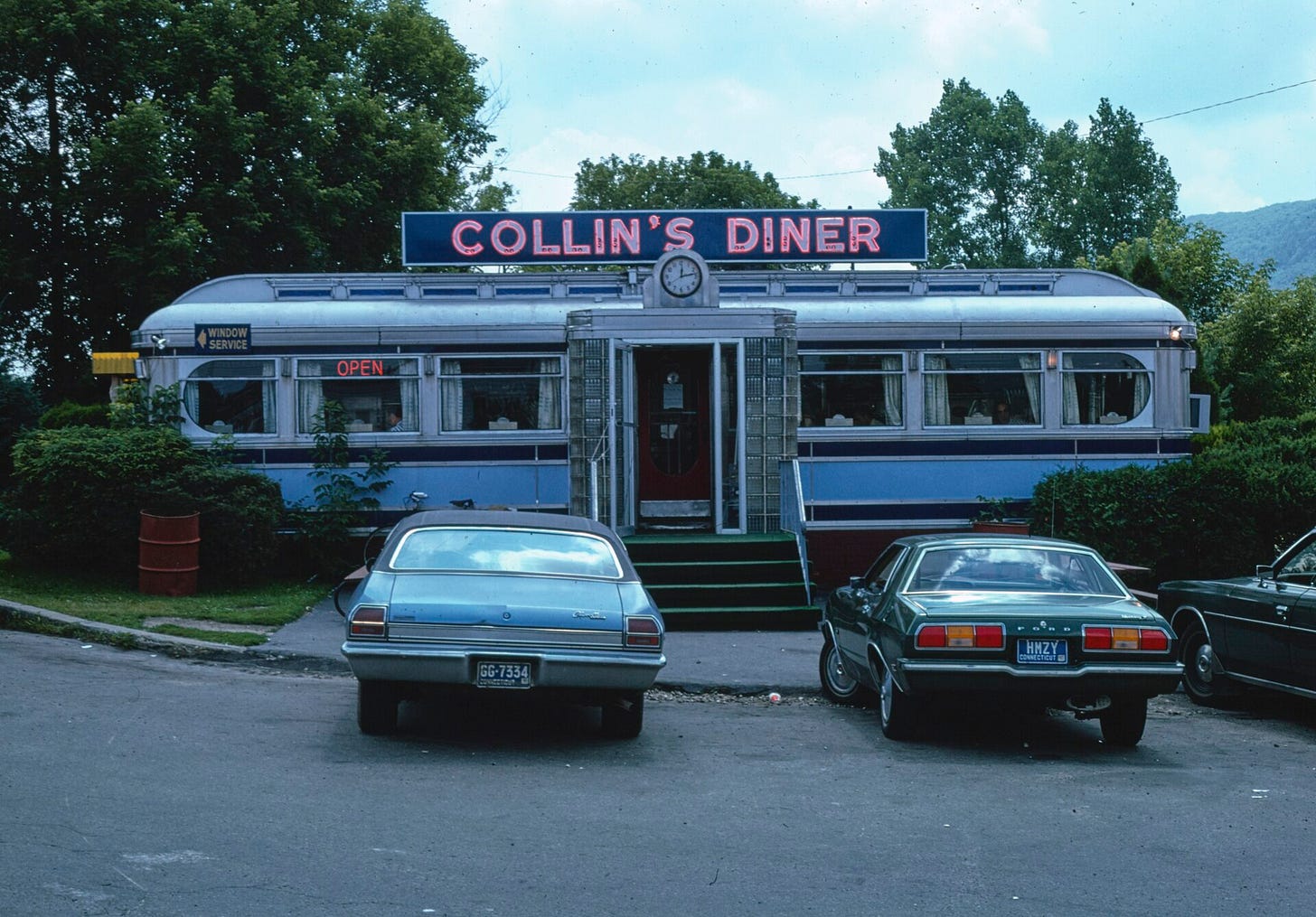 A lit corner diner with large glass windows on an empty city street at night
