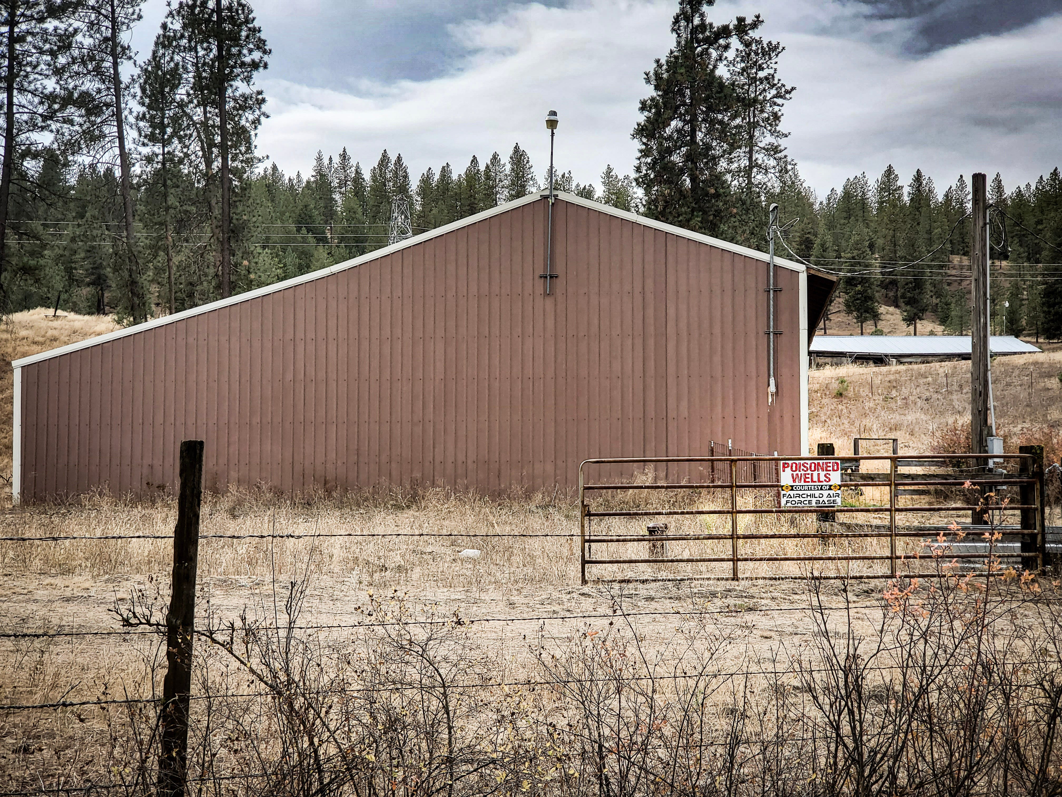 A barn and a fence with a sign reading "Poisoned Wells Courtesy of Fairchild Air Force Base"