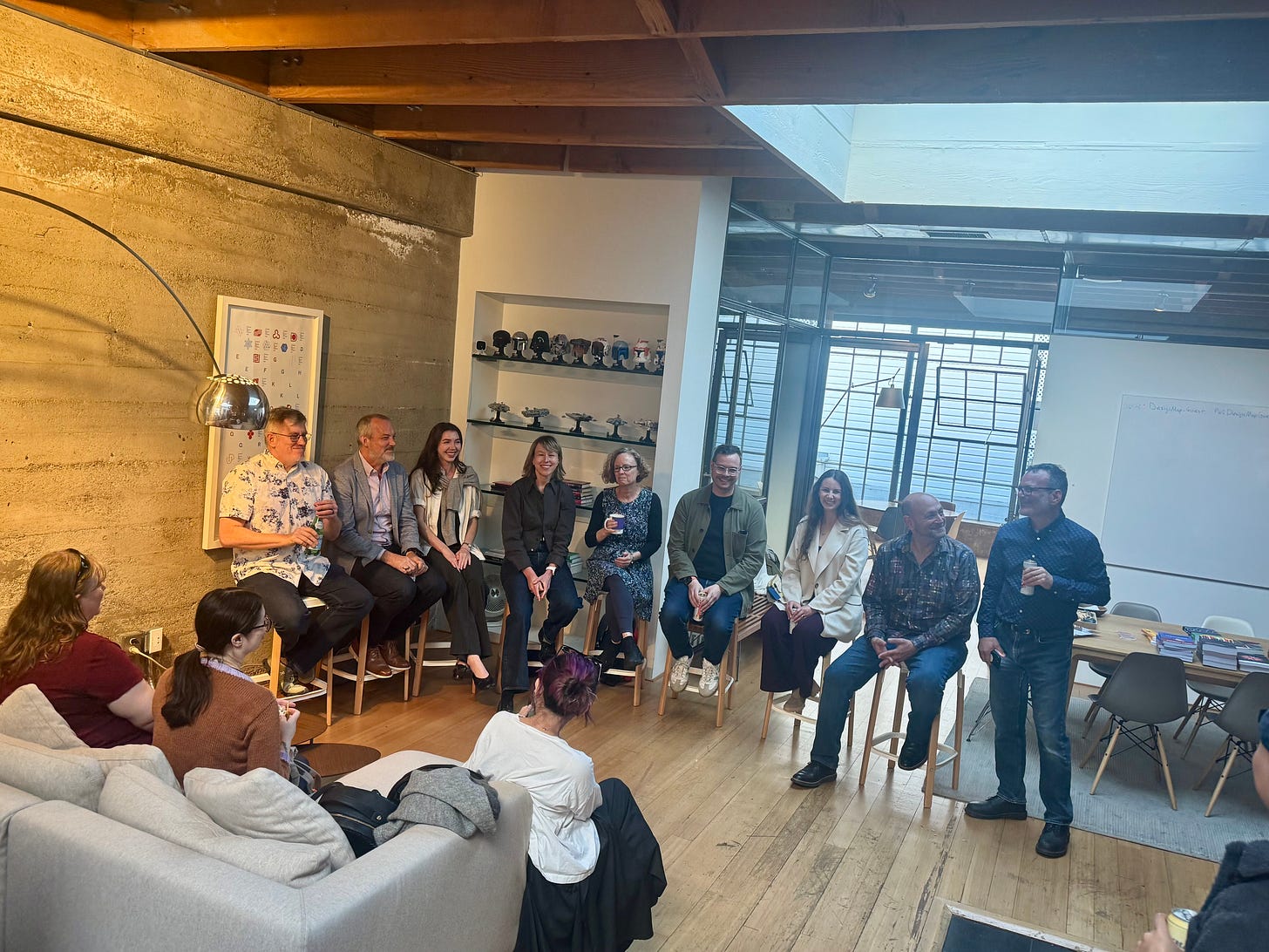 Panel of speakers seated on stools in a loft-style studio space, audience watching from couches in the foreground.