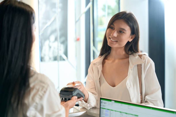 Smiling female finishing shopping in beauty salon Young lady is holding terminal where happy customer making payment with credit card Payment Management System in hotel stock pictures, royalty-free photos & images Smiling female finishing shopping in beauty salon Young lady is holding terminal where happy customer making payment with credit card Payment Management System in hotel stock pictures, royalty-free photos & images