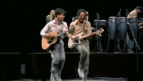 selects from Talking Heads' concert film Stop Making Sense. images of Byrne holding a microphone to camera, raising his arms, dancing in a big suit an with a lamp and full shots of the band.
