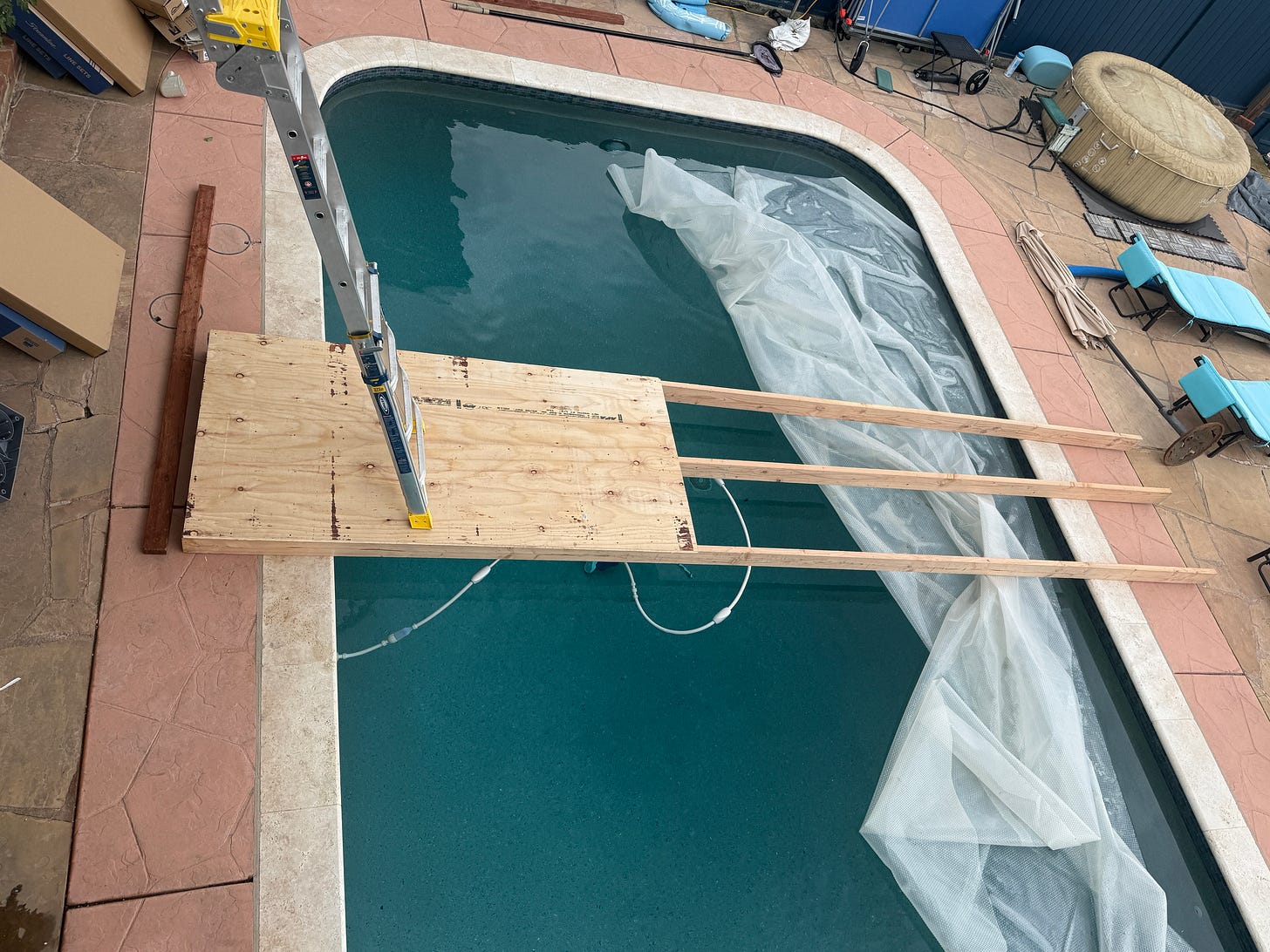 To solve the ladder problem, the installers laid long pieces of wood across the pool, and then built a platform ON the wood, so the back of the ladder is resting on a small wooden platform suspended over the pool. Bravo, guys.