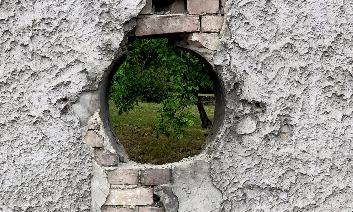 a hole in a wall, trees visible behind a hole in a wall, trees visible behind