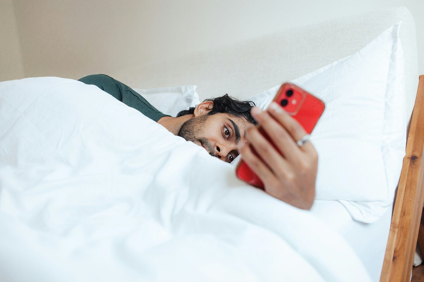 Man in bed checking his red smartphone. 