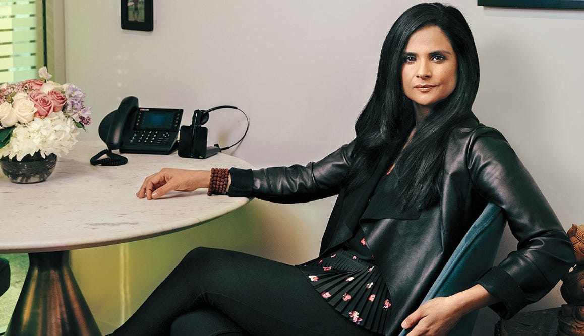 Bela Bajaria vestida toda de preto e sentada em frente a uma mesa executiva