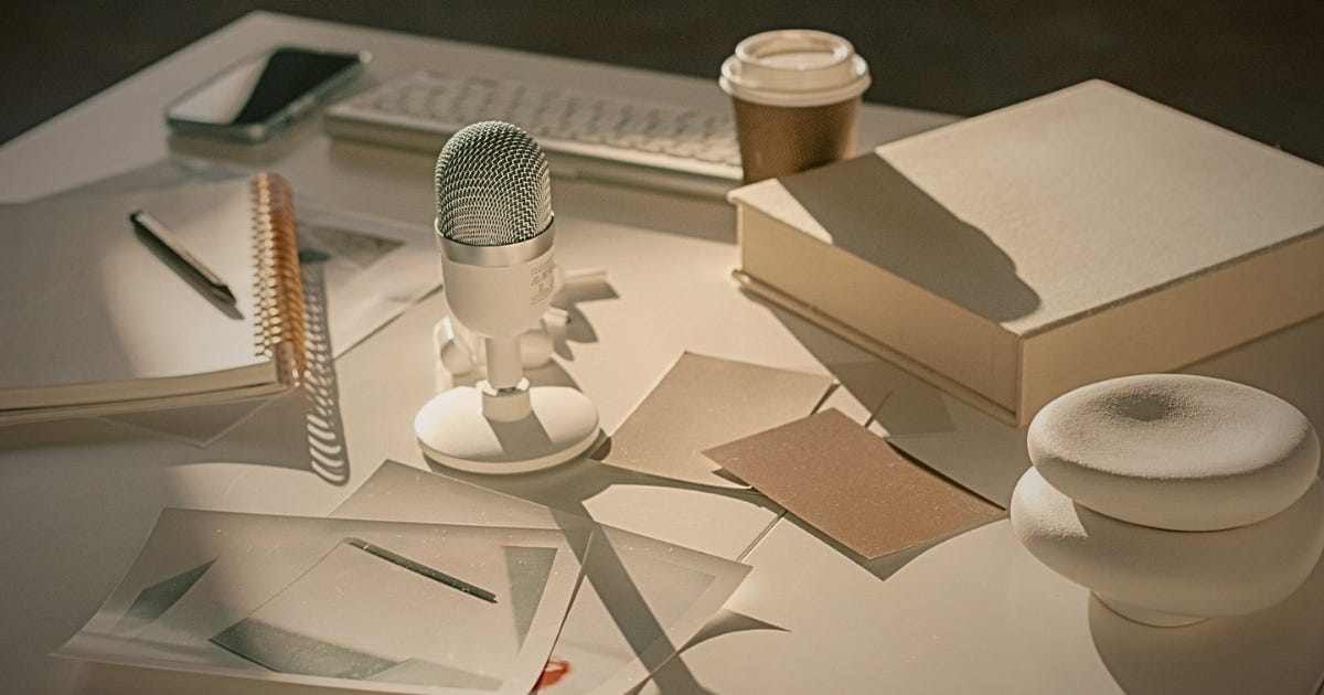 A consultant's desk with a podcast microphone, scattered papers, books and a takeaway coffee, reflecting the voice and clarity an independent consultant brings to content that reaches the right reader at the right moment.