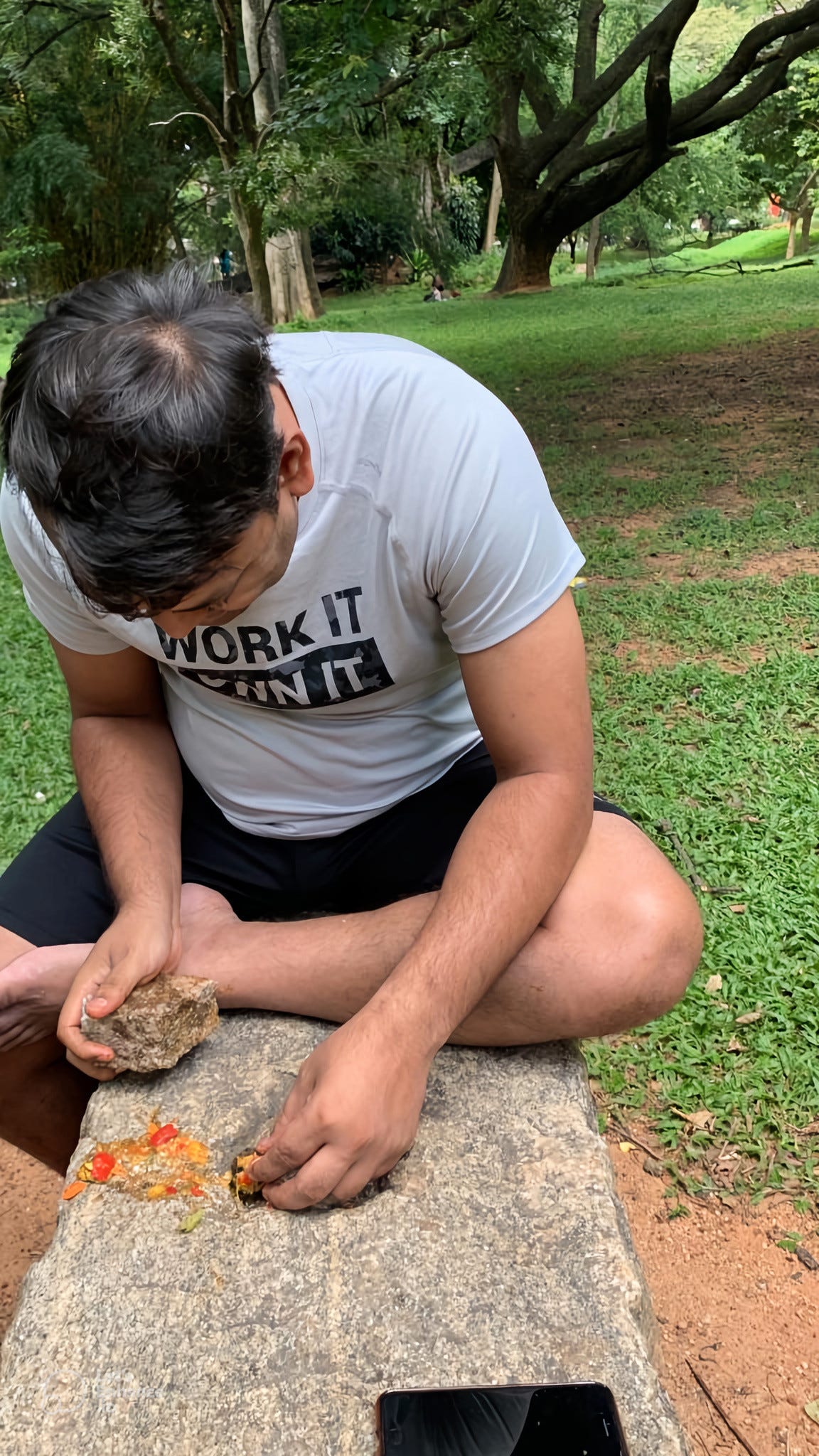A man sitting in between a green field trying to see the insides of an unknown fruit A man sitting in between a green field trying to see the insides of an unknown fruit