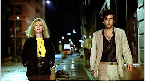 A woman and a man walk down a city street at night.