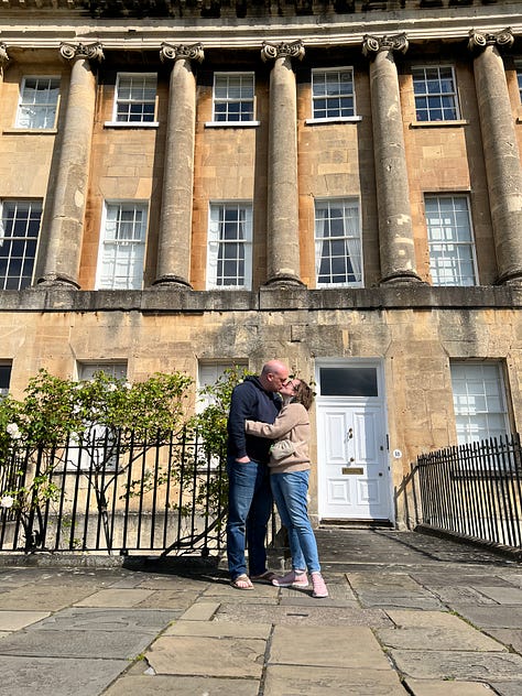 photos of Katie on vacation in London with Chris, seeing Les Mis, kissing in Bath, drinking tea, eating gluten free fish and chips, seeing a statue from DDLJ, and freezing at a football match.