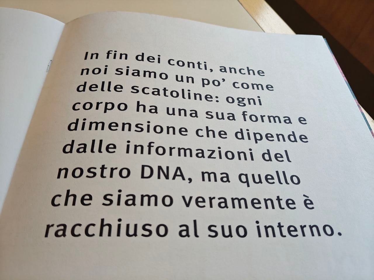 Pagina di un libro con testo in nero su sfondo beige chiaro. Il testo recita: "In fin dei conti, anche noi siamo un po' come delle scatoline: ogni corpo ha una sua forma e dimensione che dipende dalle informazioni del nostro DNA, ma quello che siamo veramente è racchiuso al suo interno."