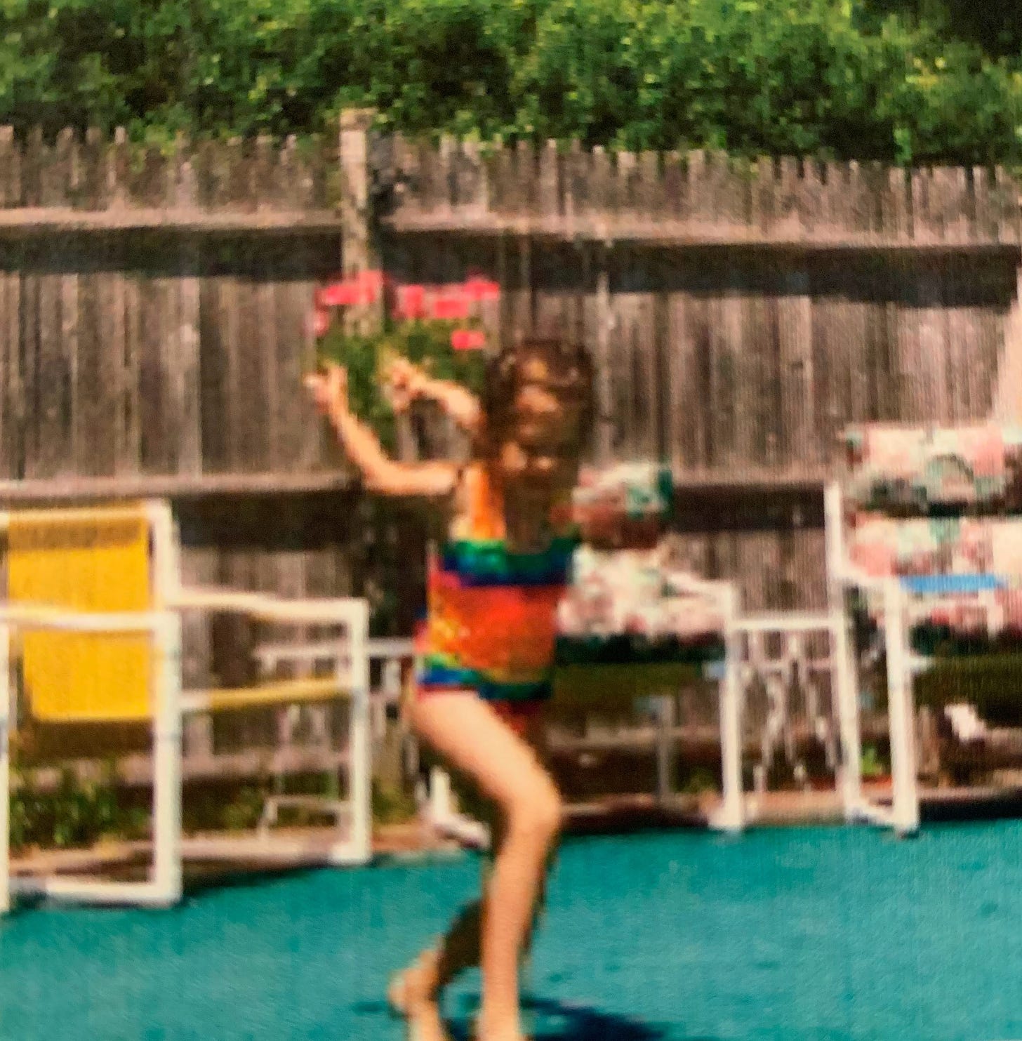A girl stands in a colorful bathing suit with her arms behind and above her at an awkward angle