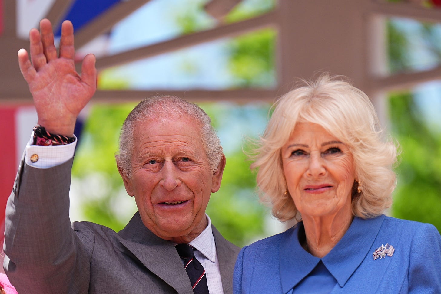 King Charles waving and Queen Camilla stood next to him smiling