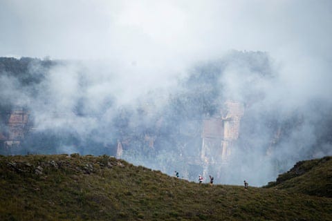 Runners make their way along a ridge, with a cloud-covered mountain looming behind them Runners make their way along a ridge, with a cloud-covered mountain looming behind them