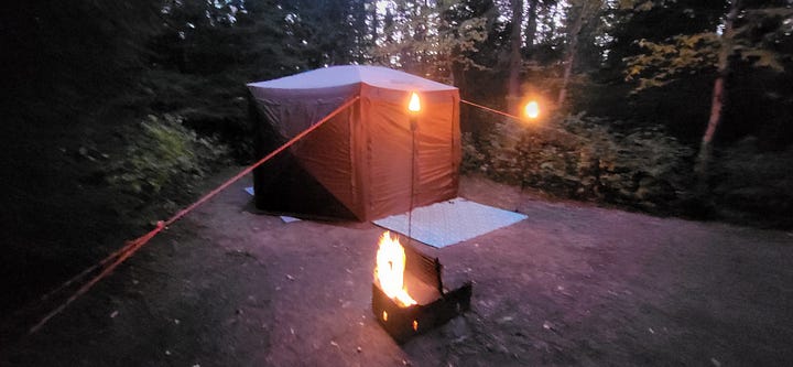 A two-photo gallery of a large beige tent at a Pukaskwa campsite. The first shows the site in bright daylight; the second shows a similar scene at night, illuminated by the warm, flickering glow of lit tiki torches.