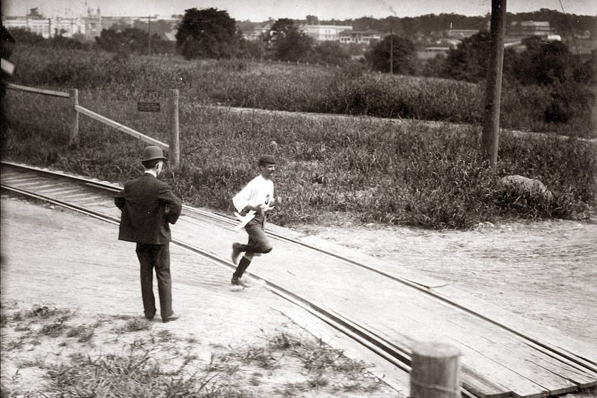 A man in a beret runs past a man in a suit