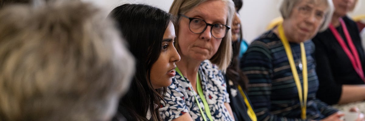 A teenage girl speaks to a group of adults, who are leaning in to listen intently A teenage girl speaks to a group of adults, who are leaning in to listen intently
