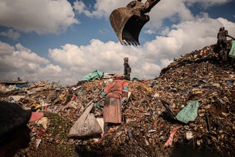 Waste pickers work next to an excavator on top of a pile of rubbish