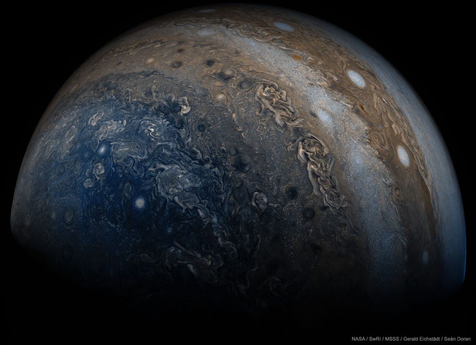 A close-up image is shown of the planet Jupiter.
Many clouds are visible including clouds colored blue
near the bottom, on the left, and white oval clouds
on the upper right. 
Please see the explanation for more detailed information.