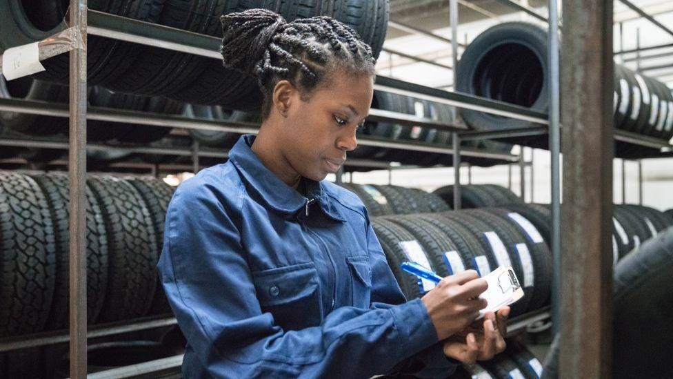 A woman at work ticking off a list with tyres behind her A woman at work ticking off a list with tyres behind her