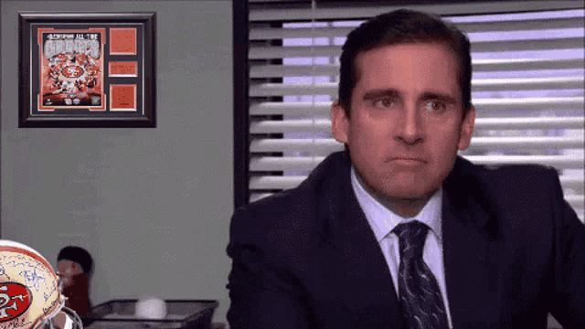 a man in a suit and tie is sitting in front of a framed poster that says " 49ers all time greats " a man in a suit and tie is sitting in front of a framed poster that says " 49ers all time greats "