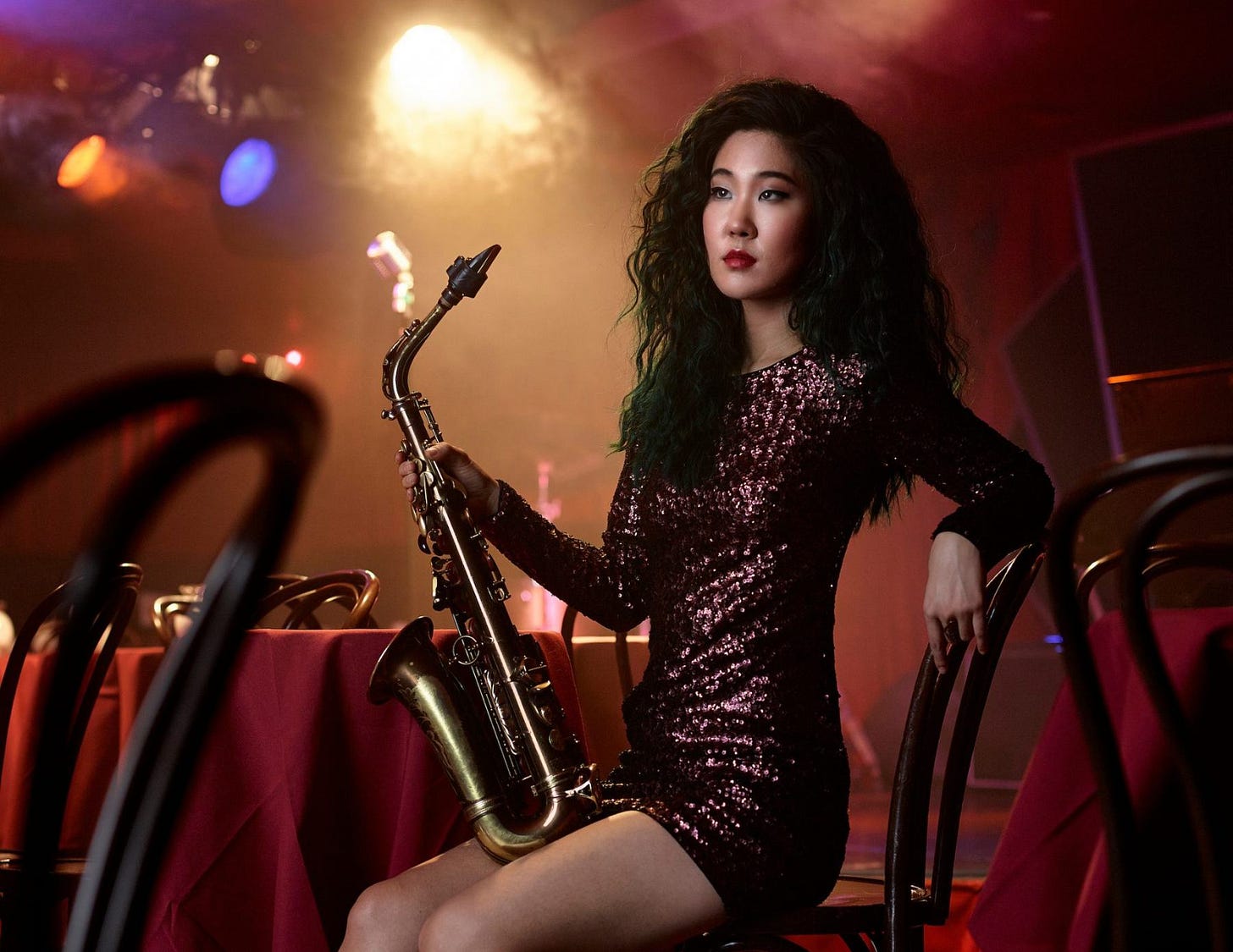 Grace Kelly sits in a darker room on a chair holding her saxophone