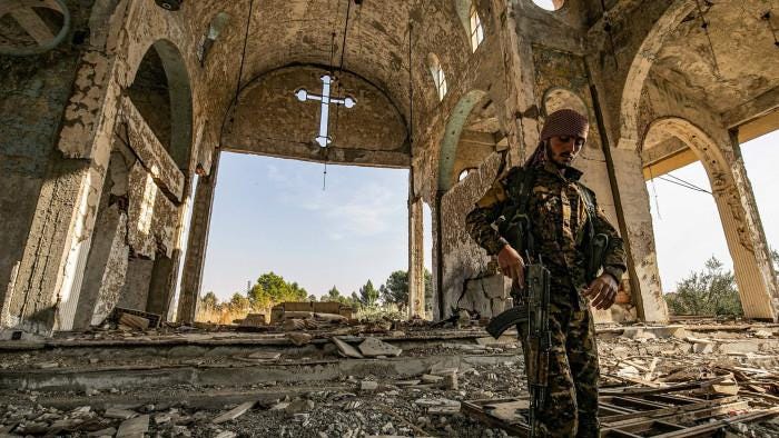 TOPSHOT - A member of the Khabour Guards (MNK) Assyrian Syrian militia, affiliated with the Syrian Democratic Forces (SDF), walks in the ruins of the Assyrian Church of the Virgin Mary, which was previously destroyed by Islamic State (IS) group fighters, in the village of Tal Nasri south of the town of Tal Tamr in Syria's northeastern Hasakah province on November 15, 2019. - The few Assyrian Christians who escaped the Islamic State group invasion in 2015, and did not choose to emigrate, now anxiously watch the advance of Turkish forces toward their villages in southern Hassakeh province. Ankara is still trying to gain ground despite two ceasefire agreements reached last month to put an end to its offensive against the Kurdish-dominated region. Turkey had launched the offensive on October 9 to push back from its border the Kurdish People's Protection Units (YPG), the backbone of the Kurdish-Arab Syrian Democratic Forces (SDF), and deemed a &quot;terrorist&quot; group by Ankara. (Photo by Delil souleiman / AFP) (Photo by DELIL SOULEIMAN/AFP via Getty Images)