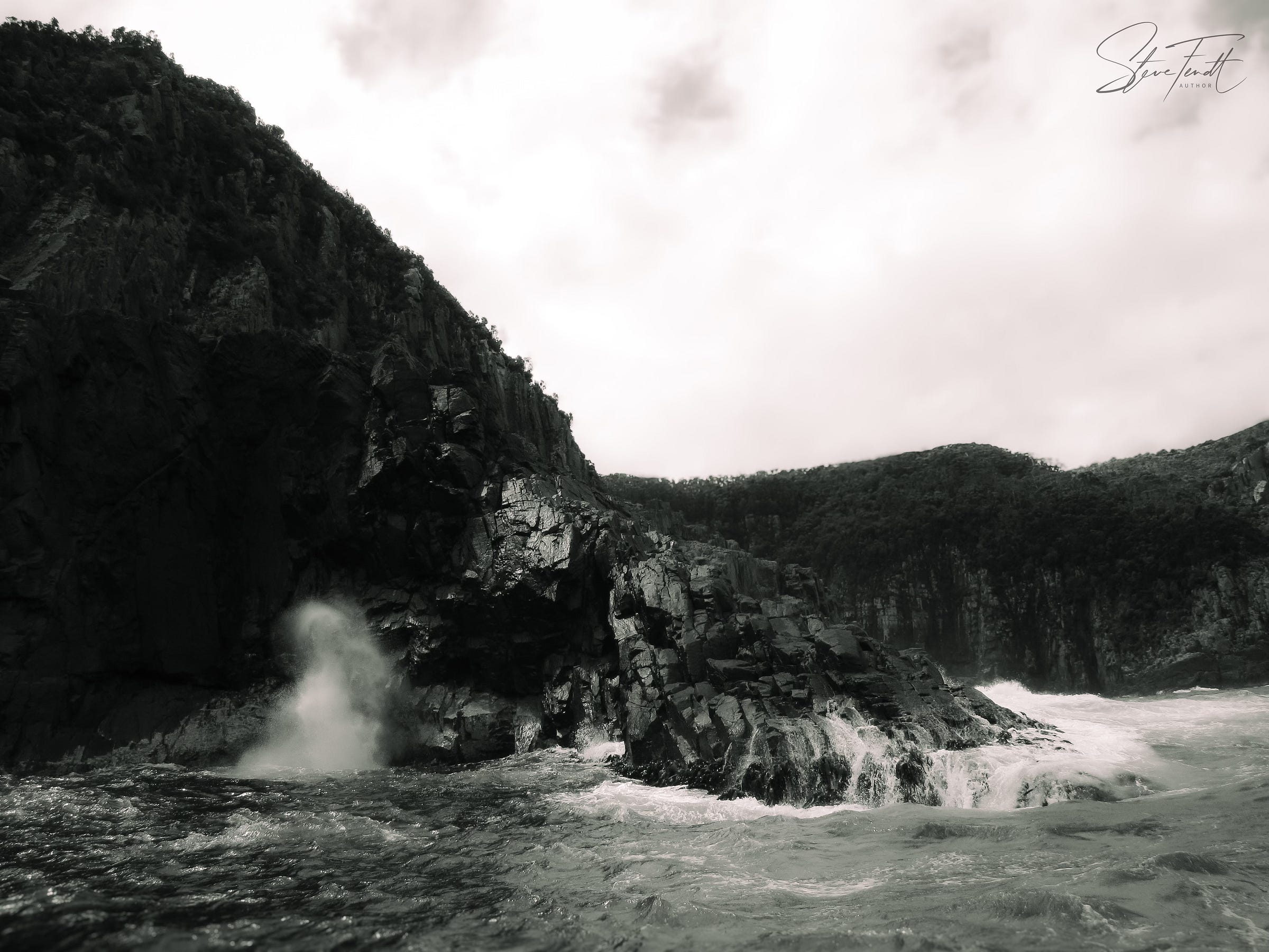 Seascape: waves swirling around the base of a cliff, spray flying.