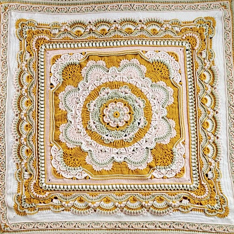 A crocheted mandala afghan blanket in goldenrod, sage, pink, and white.