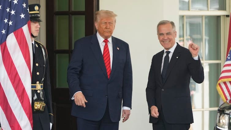 Two men stand smiling in the door way of a white stone building with American flags on either side of them. One man is corpulent with fluffy white-blond hair. The other has short grey hair and his fist is raised. Two men stand smiling in the door way of a white stone building with American flags on either side of them. One man is corpulent with fluffy white-blond hair. The other has short grey hair and his fist is raised.