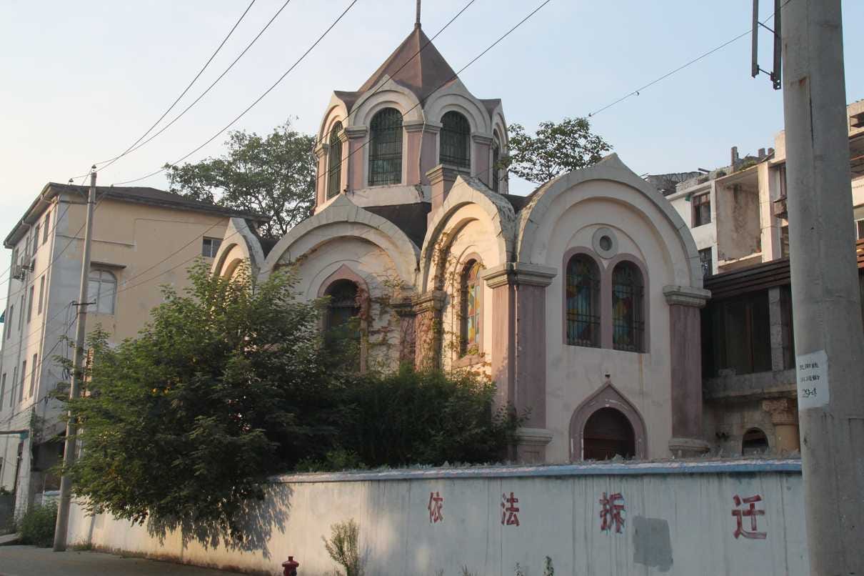 2013年修缮前的汉口东正教堂，展示粉色外墙斑驳、屋顶长满杂草的残破风貌，前方白墙写有红色“依法拆迁”字样。