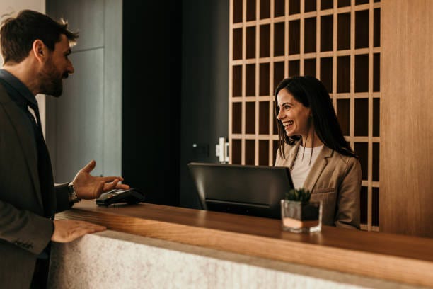 The female receptionist talking with a male customer behind the desk counter.