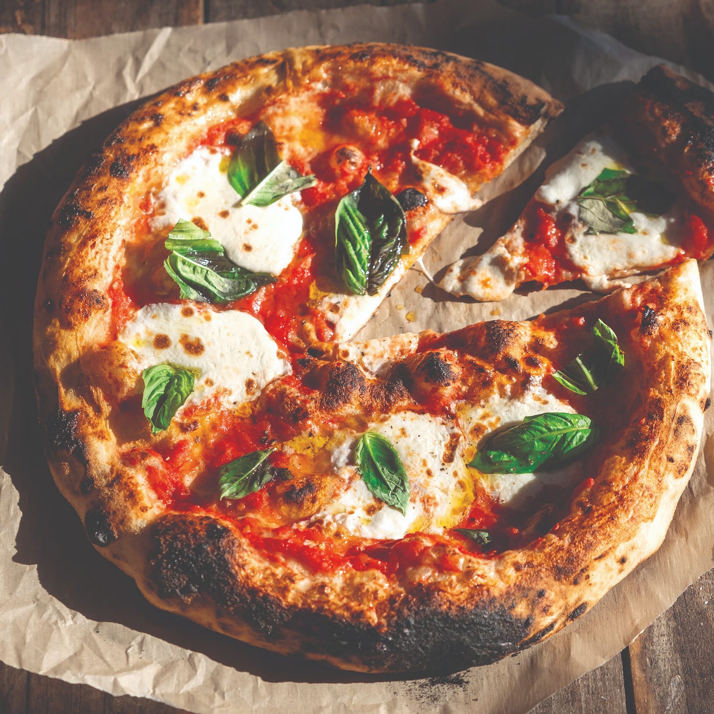 A classic margherita pizza, with a thick crust, on baking paper on top of a wooden surface A classic margherita pizza, with a thick crust, on baking paper on top of a wooden surface