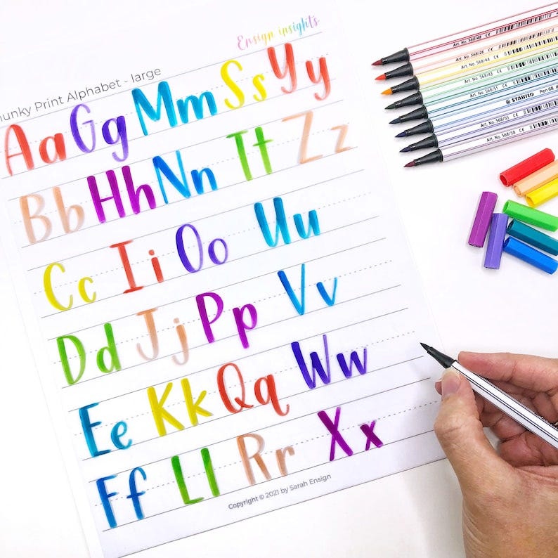 May include: A sheet of paper with a rainbow alphabet written in a chunky print style. The letters are written in different colors, with each row of letters having a different color scheme. The text "hunky Print Alphabet - large" is at the top of the page. The text "Ensign insights" is at the top right corner of the page. The text "Copyright © 2021 by Sarah Ensign" is at the bottom of the page.