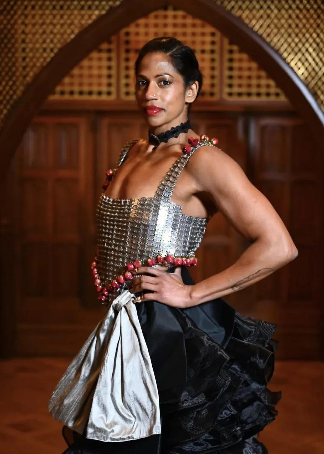 Natalie in a silver chainmail-style crop top with red beaded trim, black ruffled high-low skirt, and a thin lace choker.