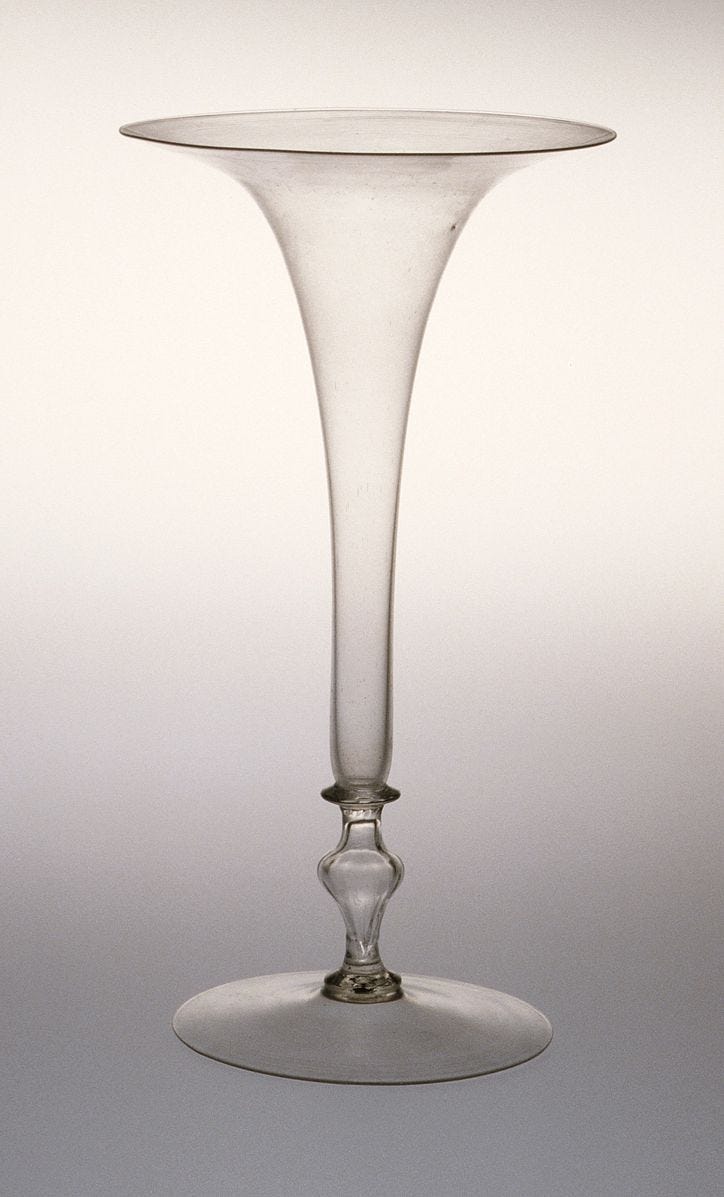 This may contain: a tall glass vase sitting on top of a white tableclothed flooring with a gray background This may contain: a tall glass vase sitting on top of a white tableclothed flooring with a gray background