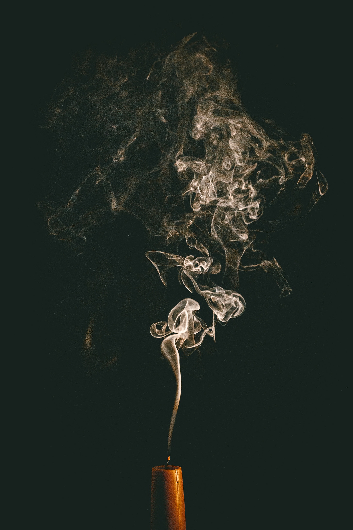 smoke rising from a recently extinguished caramel-coloured candle, black background
