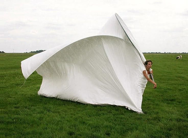 This may contain: a woman standing next to a giant white object in a field