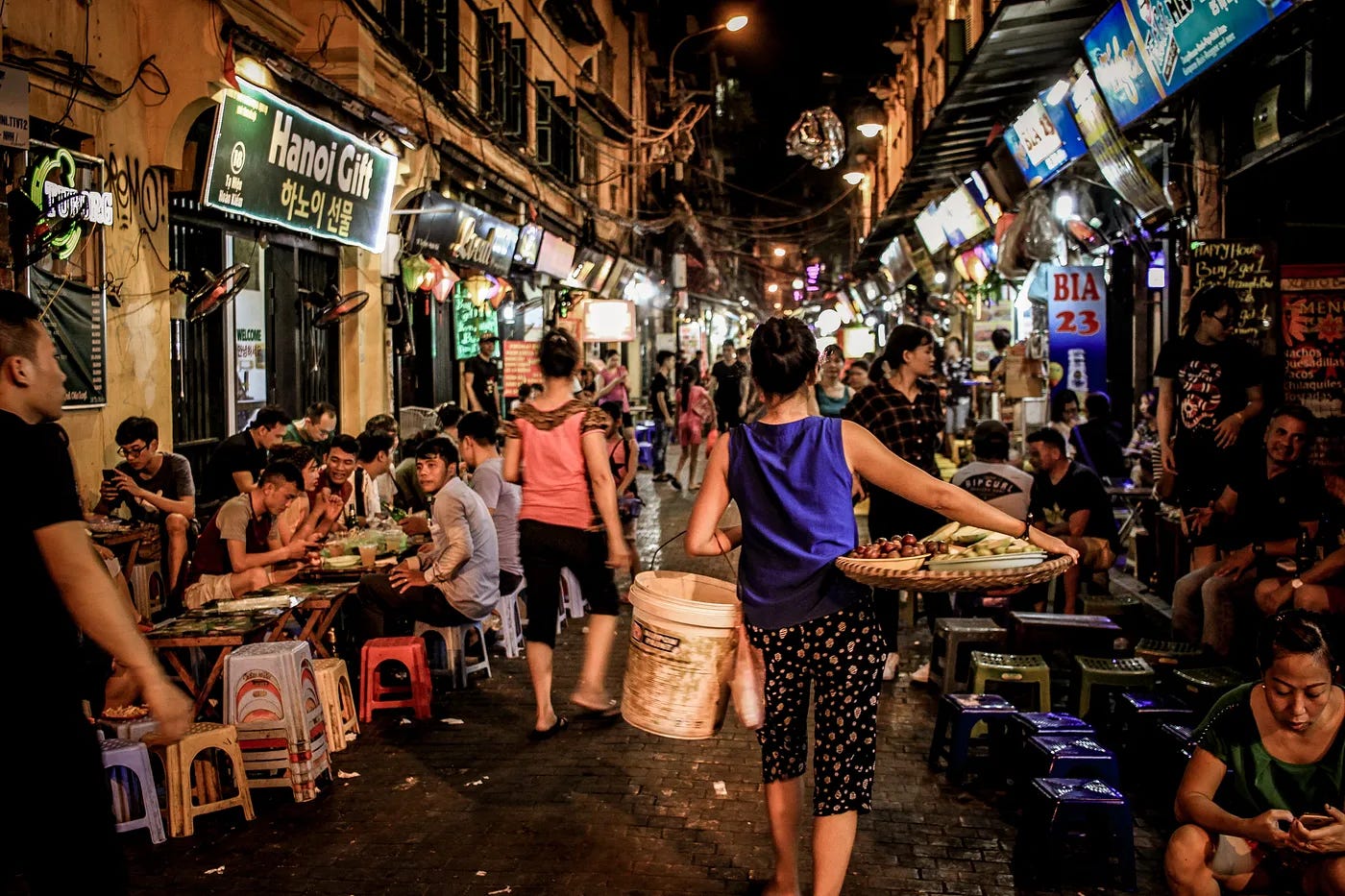Women walking and men drinking in a crowded narrow street in Hanoi Women walking and men drinking in a crowded narrow street in Hanoi
