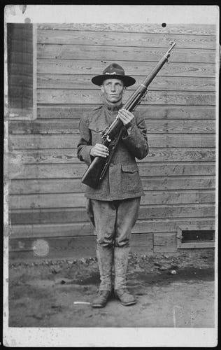 An unidentified U.S. Army soldier in World War I uniform stands outside an unpainted wooden building, holding an M1917 Enfield rifle diagonally across his chest. Naval History and Heritage Command photograph NH 105113. An unidentified U.S. Army soldier in World War I uniform stands outside an unpainted wooden building, holding an M1917 Enfield rifle diagonally across his chest. Naval History and Heritage Command photograph NH 105113.